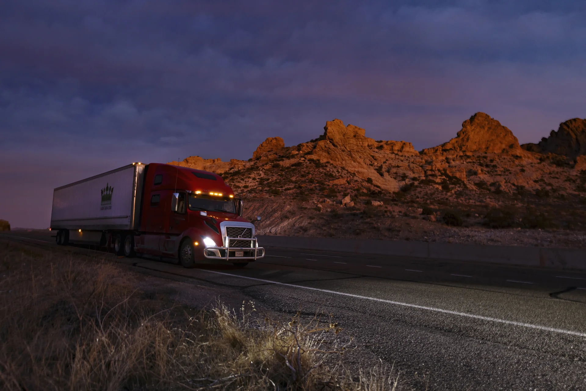Red Volvo sleeper truck on a highway in the Arizona desert at dusk